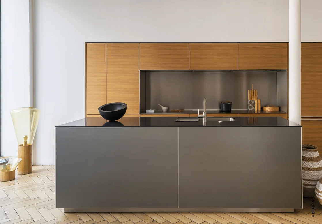 Inspiration BRADANO — Cuisine avec un grand îlot anthracite, un évier intégré au plan sombre et des rangements ton bois en arrière-plan.